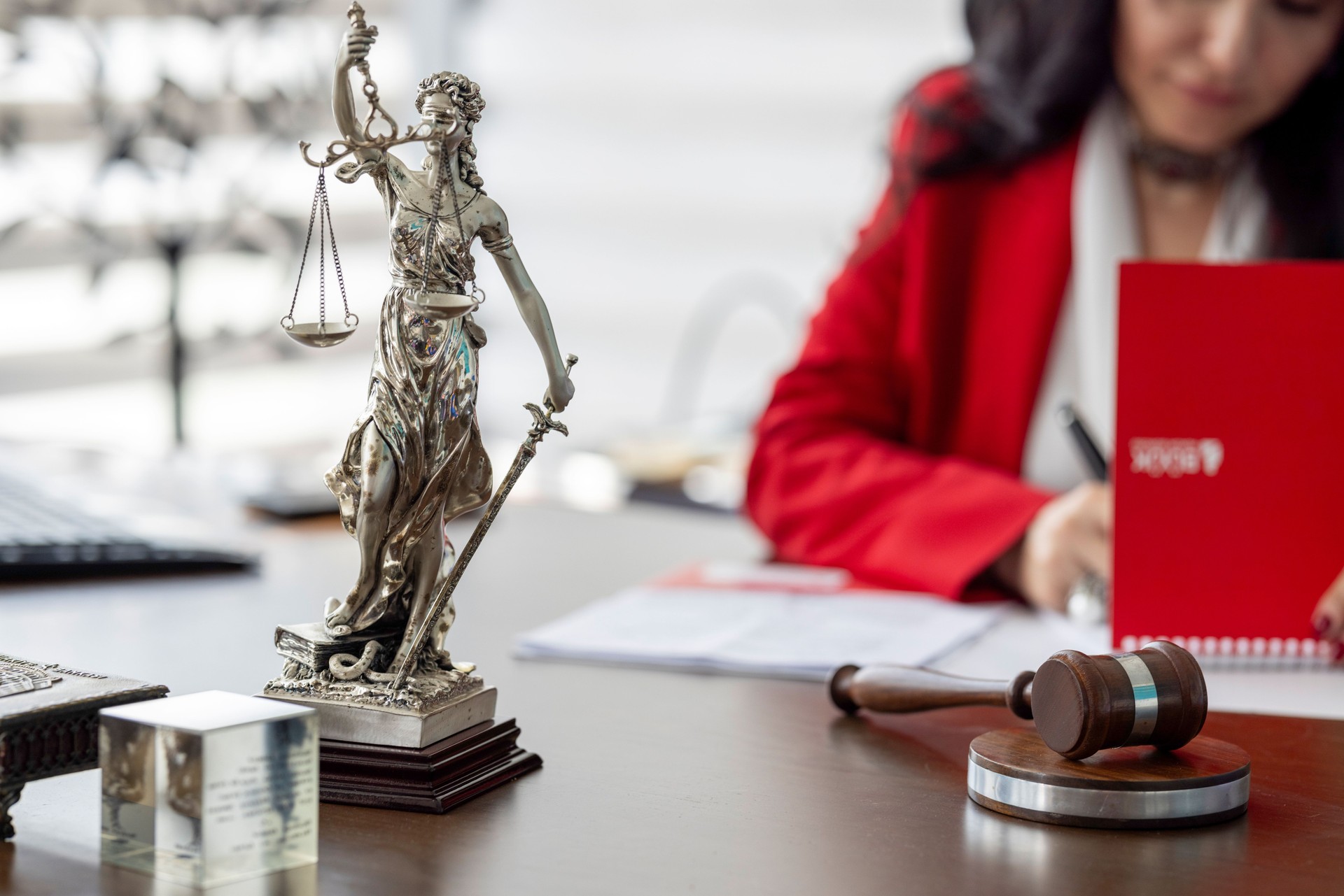 Law and justice concept. Female lawyer in red jacket working in office, writing note on paperwork.